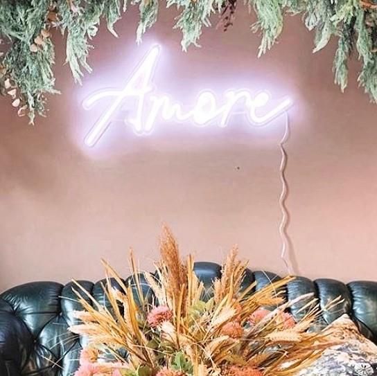 Amore CUSTOM NEON® sign in white LED neon flex shown wall mounted above a couch