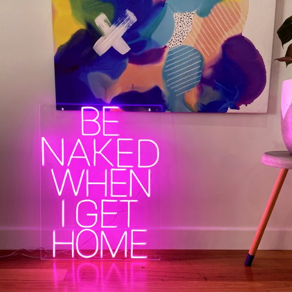 Be Naked When I Get Home LED neon sign shown on the floor beneath a painting - photo from CustomNeon.co.uk
