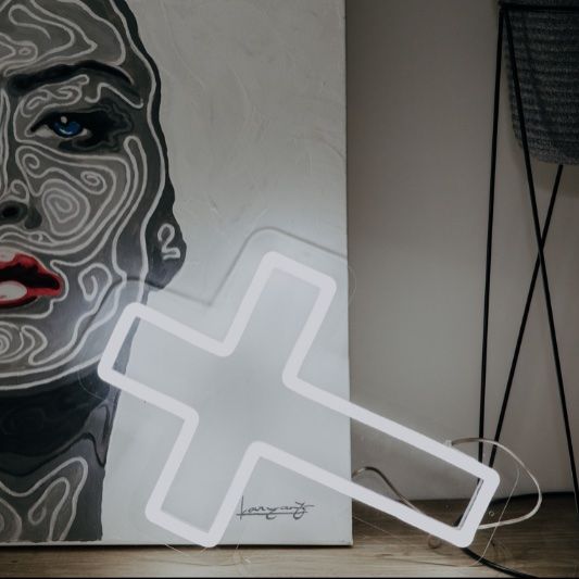 LED neon cross shown in white against a painting - photo from CustomNeon.co.uk