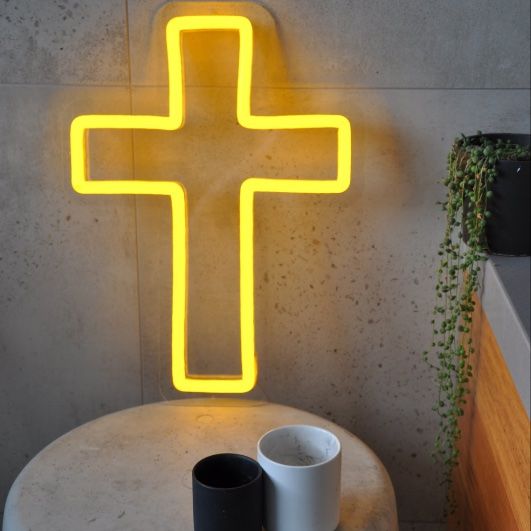 LED neon cross shown illuminated in yellow on a side table - photo from CustomNeon.co.uk