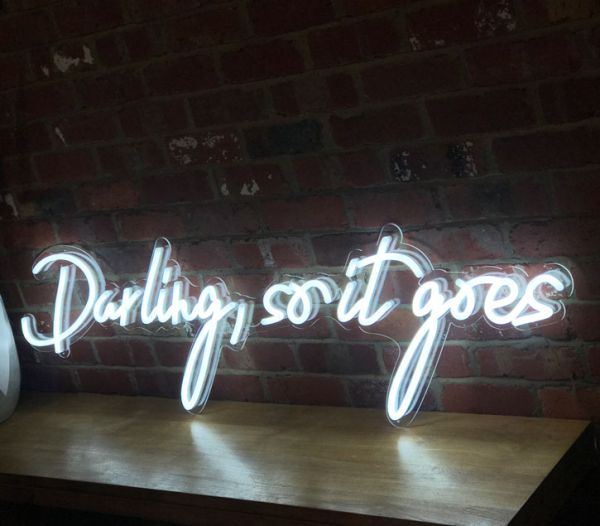Beautiful cursive neon word sign * Darling, so it goes * shown against exposed brick wall
 - photo from CustomNeon.co.uk