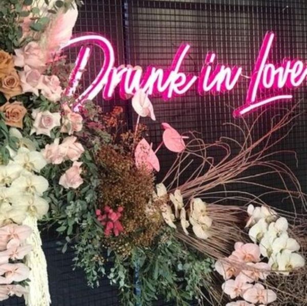 Large LED neon sign Drunk in Love attached to a mesh frame surrounded by floral decorations at an event - from Custom Neon®