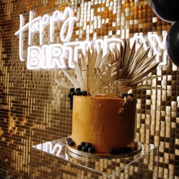 Custom Neon® Happy Birthday sign in white LED neon flex on a golden shimmer wall behind a birthday cake @raspberrycraftsandevents.