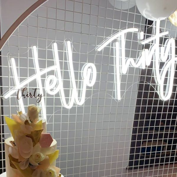Hello Thirty Light Up Birthday Sign shown in white on mesh in front of the birthday cake - photo from CustomNeon.co.uk