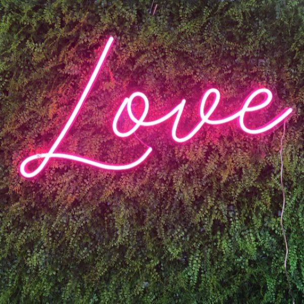 Pink Love Sign in LED neon flex shown on a natural green wall from CustomNeon.com