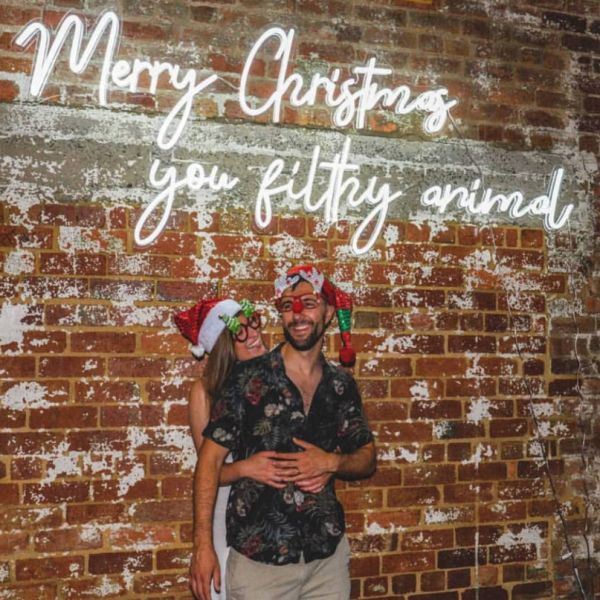 Merry Christmas You Filthy Animal LED Neon Sign shown on an exposed brick wall at a Xmas party - photo from CustomNeon.co.uk