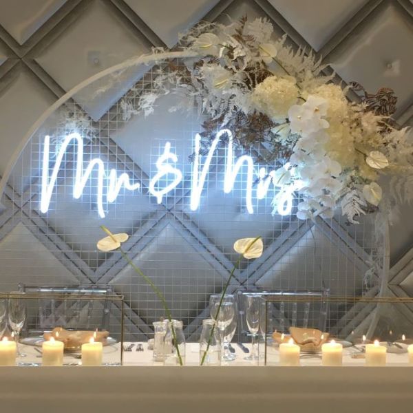 Mr & Mrs light sign in white on a floral arch behind the top table - from Custom Neon