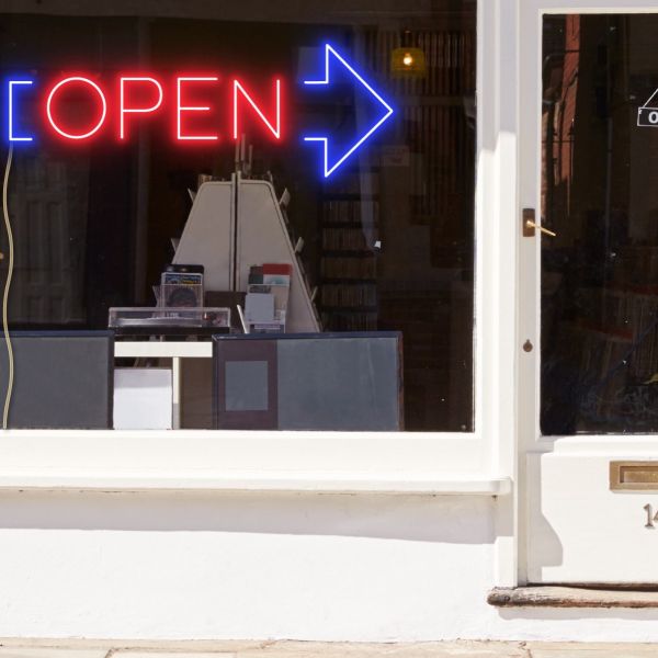Neon light open sign in red with an oversized blue arrow shown in a shop window - from CustomNeon.co.uk