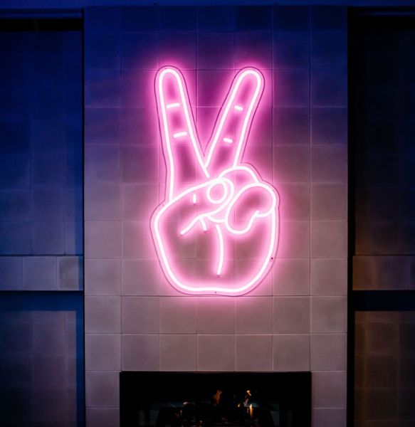 LED Neon Peace Sign Wall Art shown mounted above a fireplace - photo from @CustomNeon