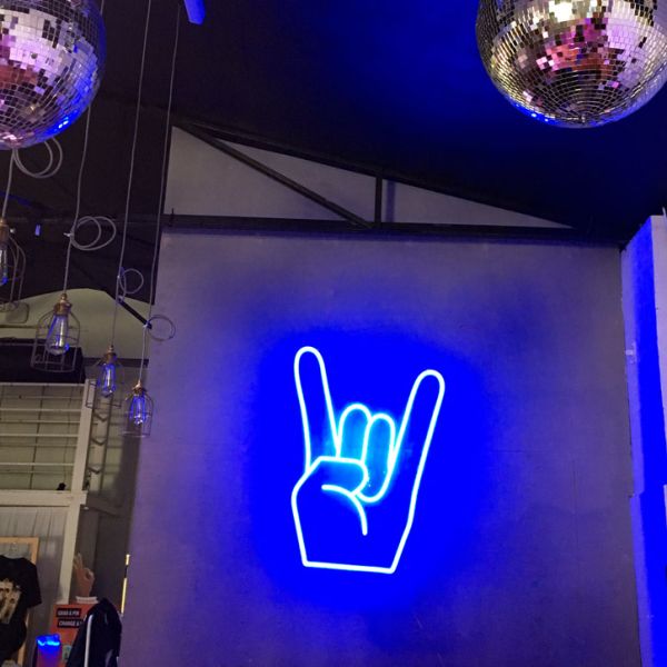 Rock On Emoji LED Neon Sign shown in blue, wall mounted in a fashion store - photo from CustomNeon.co.uk