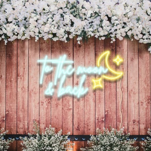 To the Moon & Back light sign with a moon & stars on a wooden fence with flowers designed by Custom Neon