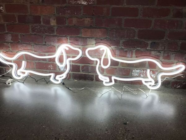 Two sausage dog neon lights shown nose to nose in front of an exposed brick wall - photo from CustomNeon.co.uk