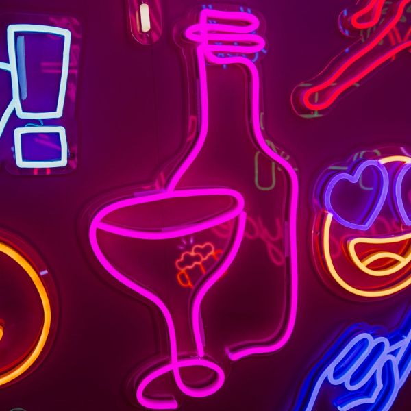 Custom Neon® Wine Glass & Bottle Line Art shown in pink illuminated against a dark pink wall in dim light
