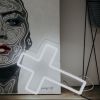 LED neon cross shown in white against a painting - photo from CustomNeon.co.uk