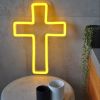 LED neon cross shown illuminated in yellow on a side table - photo from CustomNeon.co.uk