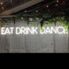 EAT DRINK DANCE large LED neon sign for events & weddings, shown on wire mesh with floral arrangement & fairy lights - photo from CustomNeon.co.uk