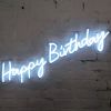 * Happy Birthday * is a lightweight, portable neon sign in modern cursive font, shown against a brick wall. Photo from CustomNeon.co.uk
