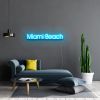 Miami Beach Light Sign by CUSTOM NEON® shown in ice blue against dark grey wall above grey blue couch