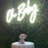 Oh Baby white LED neon sign shown on a green wall above a baby shower cake @CustomNeon.uk