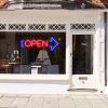 Neon light open sign in red with an oversized blue arrow shown in a shop window - from CustomNeon.co.uk