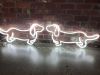 Two sausage dog neon lights shown nose to nose in front of an exposed brick wall - photo from CustomNeon.co.uk