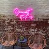 You Can't Sit with Us pink LED sign on a brick wall above chairs from Custom Neon