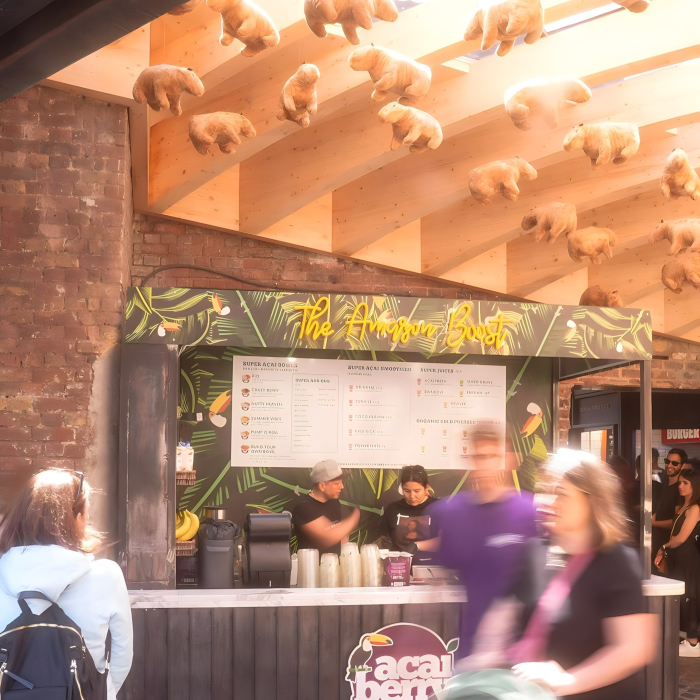 Custom Neon® The Amazon Boost sign on a wooden kiosk underneath capybara plush toys @acaiberryfoods in Camden Market