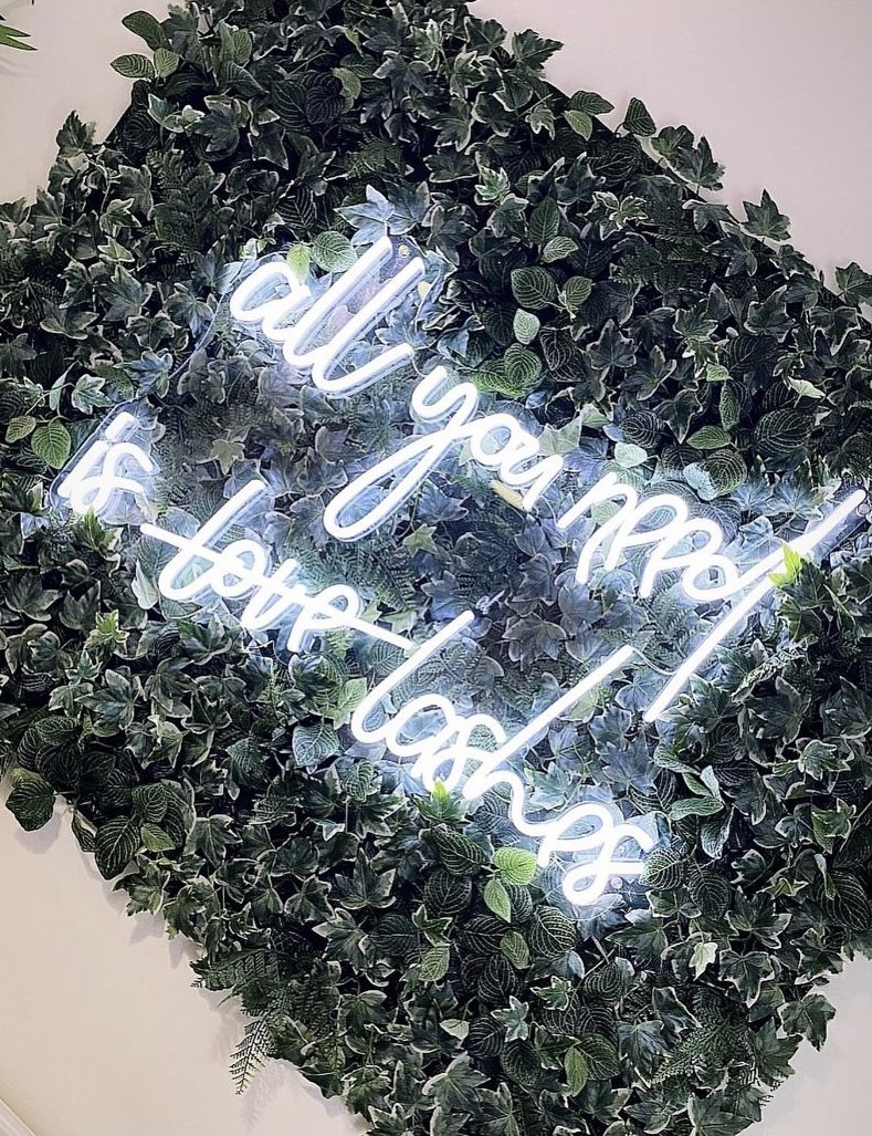 Custom Neon® white lash studio sign on lush green wall @lashedbysarahox