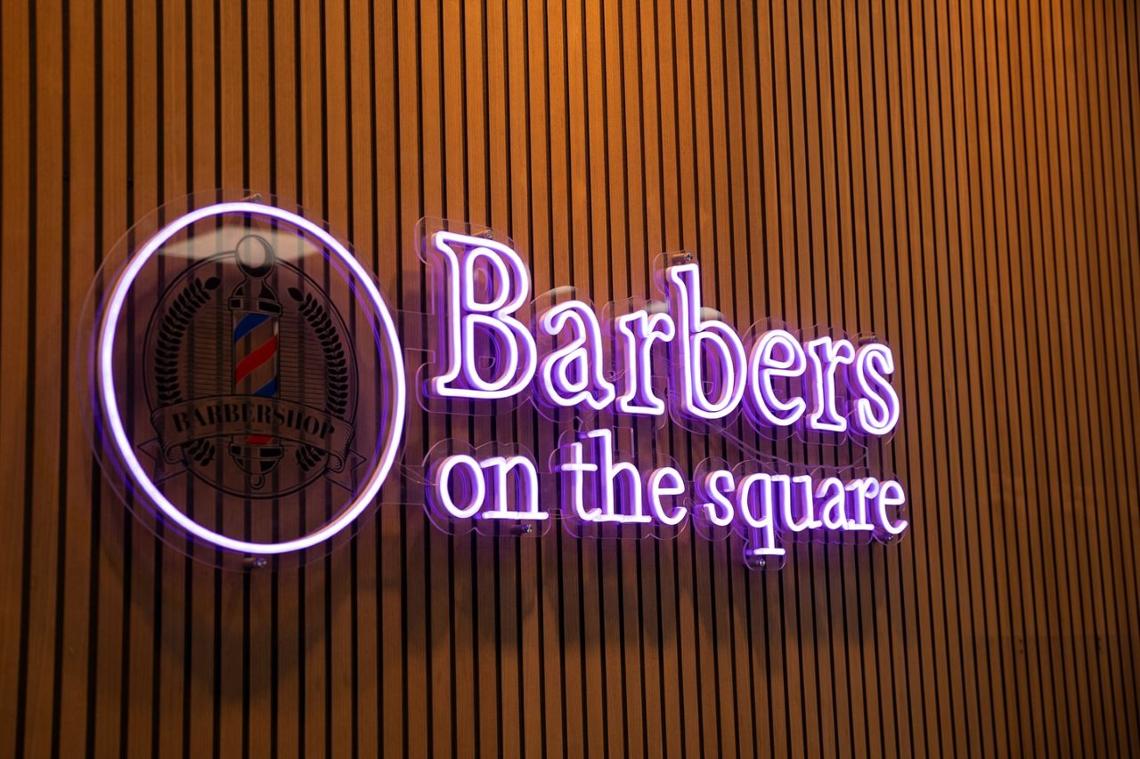 Barbers on the Square purple Custom Neon® logo sign on a wood pannelled wall