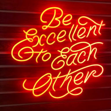 Be Excellent to Each Other red Custom Neon® quote sign on white wood paneled wall