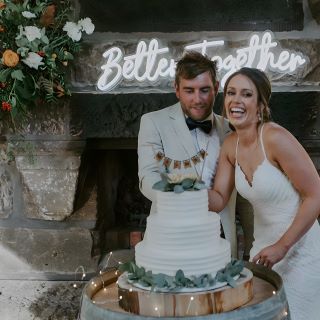 Better Together Custom Neon® wedding quote sign mounted on a stone fireplace behind the newlyweds