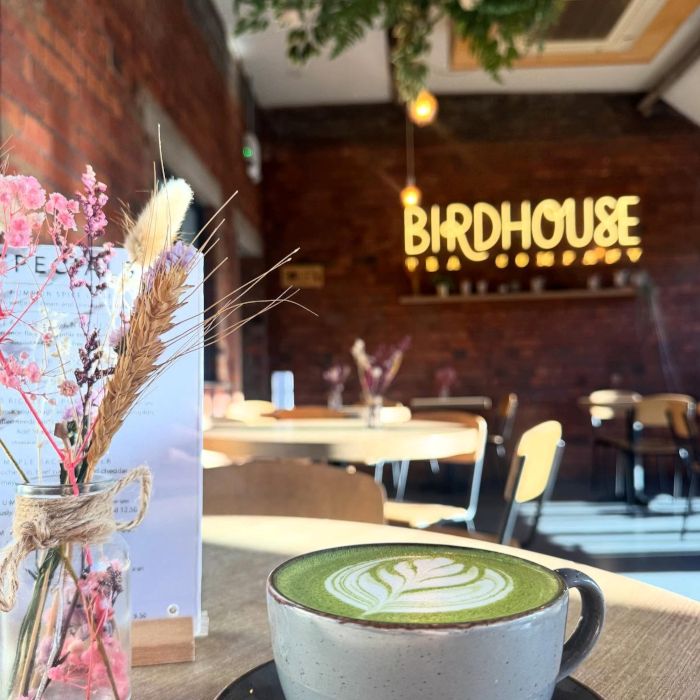 A cup of matcha latte and a floral arrangement with a large golden Custom Neon® sign in the background @birdhouseteacompany