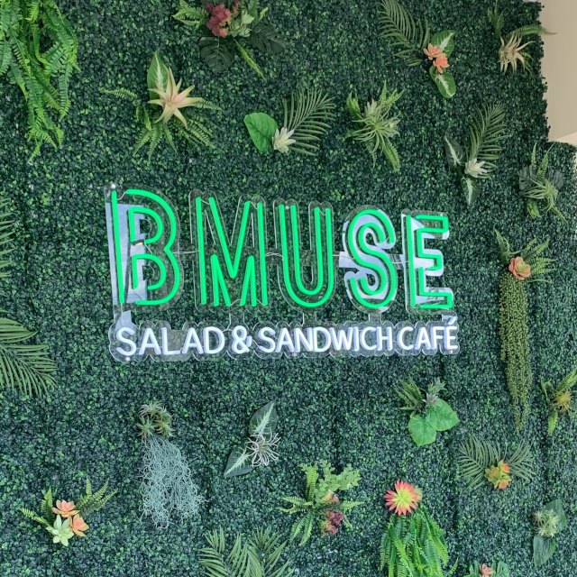 Green and white Custom Neon® logo sign on a grass wall @bmusecafe.middlebury