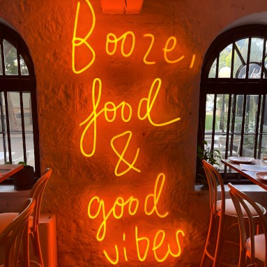 Booze Food & Good Vibes large Custom Neon® in orange LED neon mounted on a brick wall @justinlaneest
