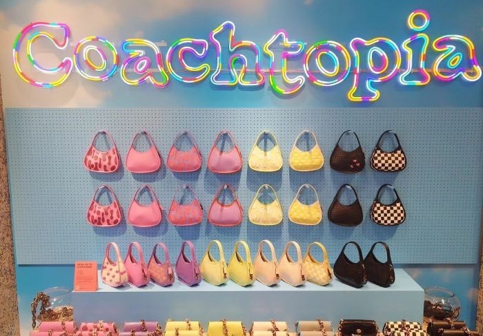 Multicolour LED neon Coachtopia logo sign above a retail display of Coach handbags
