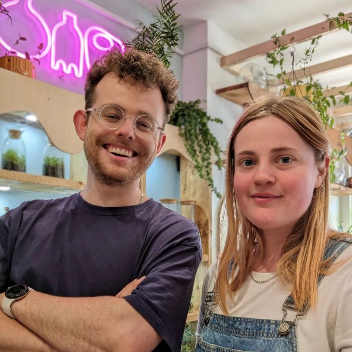 Pink Custom Neon® artwork on the wall behind two staff members of the OME Home plant shop in Bristol