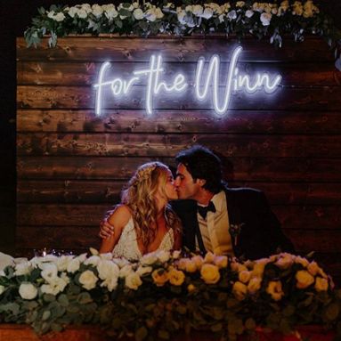 Custom Neon® pun wedding signs on a rustic wooden slat wall behind the bride and groom at a garden wedding