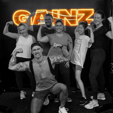 Custom Neon® dark yellow GAINZ sign on black wall behind gym goers @bodiesbyphil613