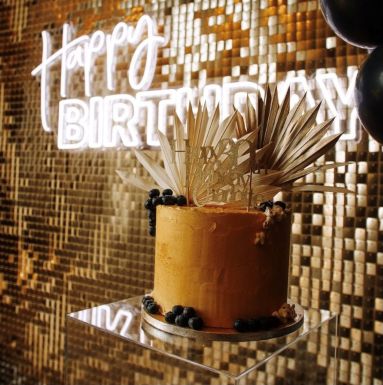 White Custom Neon® Happy Birthday sign on a golden shimmer wall styled by @raspberrycraftsandevents