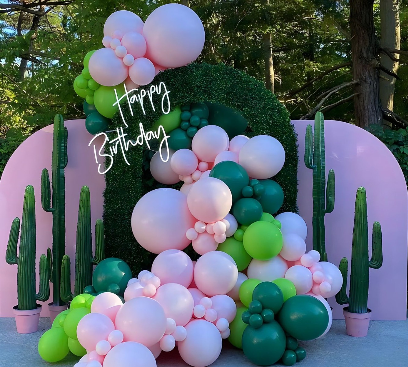 Custom Neon® Happy Birthday sign on a faux grass arch with balloons cascading through surrounded by cacti props - event decor by @decorandfiesta