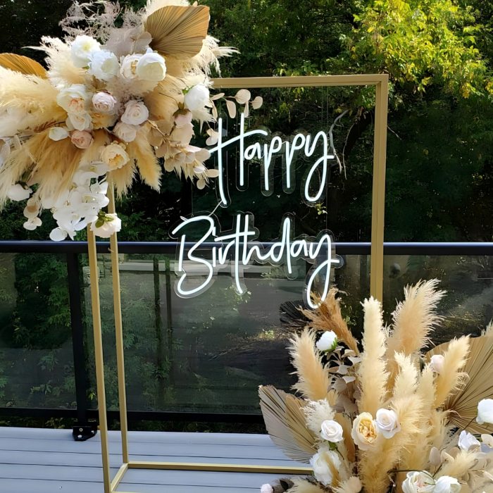 Custom Neon® Happy Birthday sign hung from a gold rectangular frame adorned with florals and pampas grass in neutral tones - event decor by @decorandfiesta
