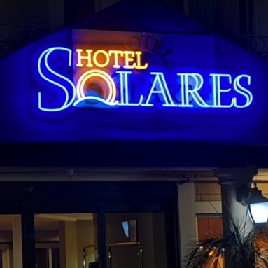 Dark blue and yellow Custom Neon® sign above the entrance to hotelsolares.com