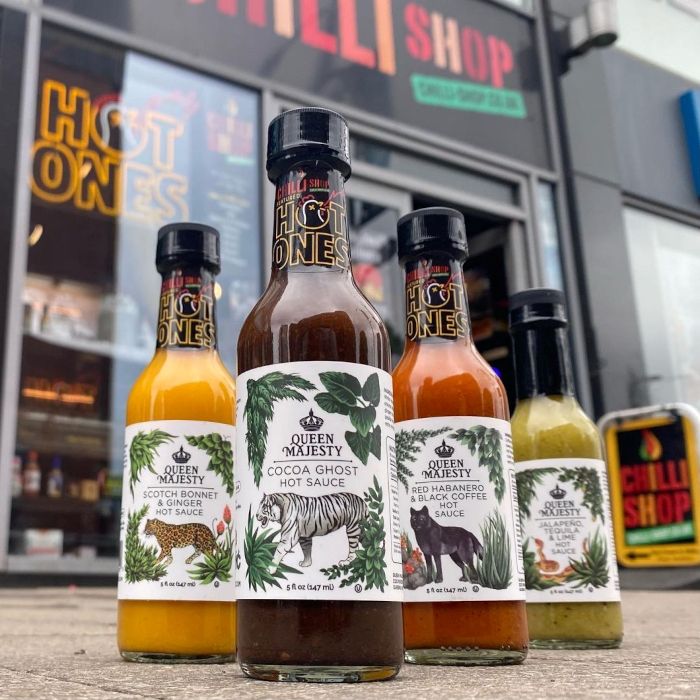 Bottles of Hot Ones brand chilli sauce on the pavement in front of The Chilli Shop with a Hot Ones Custom Neon® sign in the window