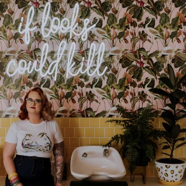 White Custom Neon® sign in a script font on a wallpapered wall in a hair salon @dollsandsailors