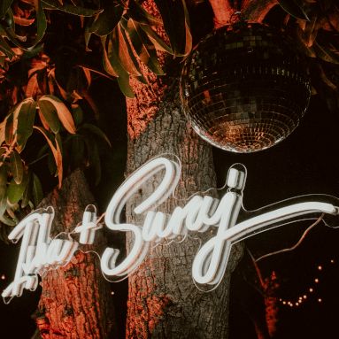Custom Neon® couples names sign for hung on a tree amidst disco balls at a lavish outdoor wedding