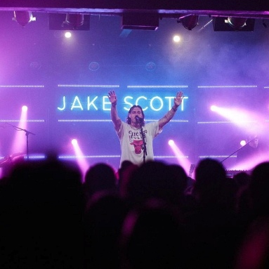 Custom Neon® white personalized stage sign behind the artist during a concert @jakescottmusic