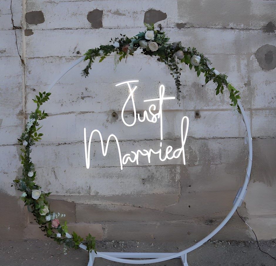 Custom Neon® Just Married sign attached to an arch stand in front of a grey concrete wall