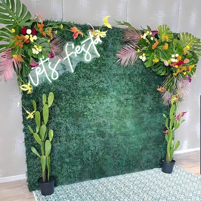Custom Neon® Let's Fiesta sign attached to a green wall decorating with monstera leaves, flowers and cacti - props and styling by @decorandfiesta