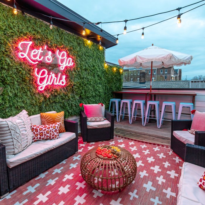 Let's Go Girls pink Custom Neon® sign in a script font on a grasswall in an outdoor area of an Airbnb designed by Somerled