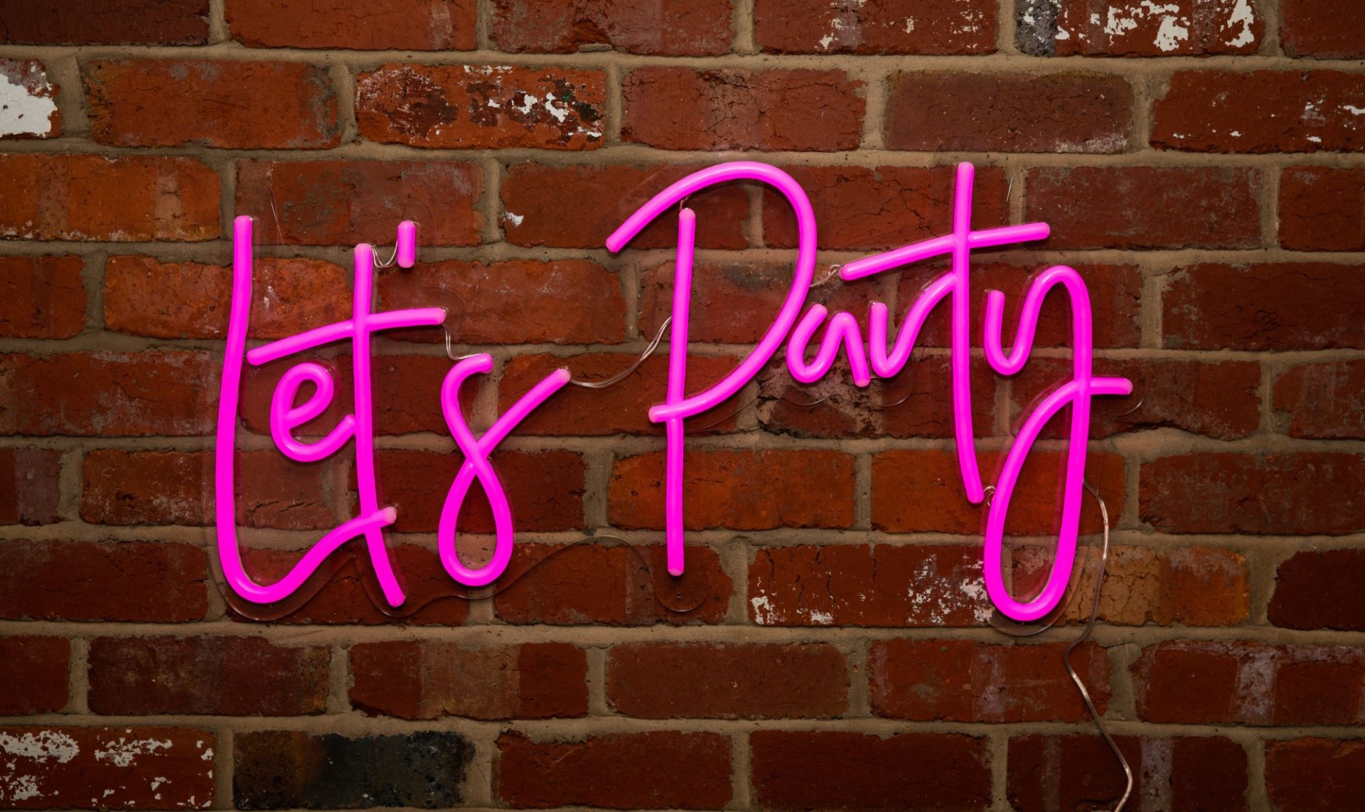Custom Neon® pink Let's Party sign mounted on a partially distressed brick wall